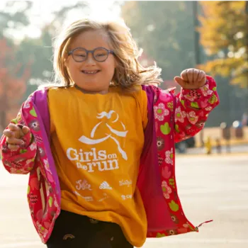 A girl smiles wearing a Girls on the Run shirt. 