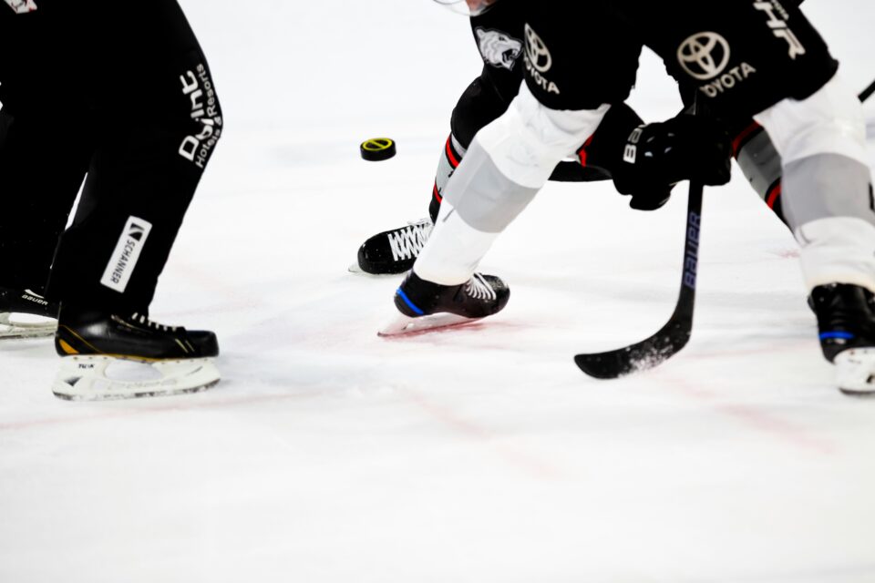 A close-up of skates and hockey sticks are shown in an action shot. 